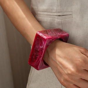 Detail of square acrylic bangle featuring deep magenta marble texture on a beige background