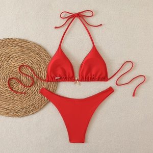 Flat lay of a bright red bikini set with a gold starfish charm on textured mat