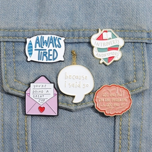 Close-up of five colorful enamel letter pins attached to a blue denim jacket pocket