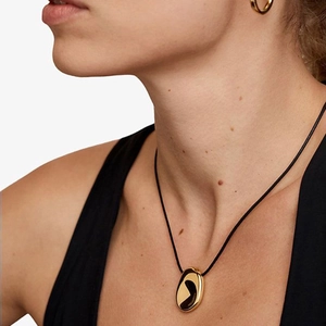 Close-up of a golden oval pendant with black inlay on a slim black cord necklace