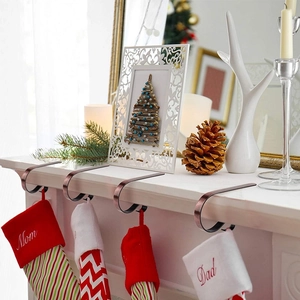 Set of 4 bronze Christmas stocking hooks displayed on a mantelpiece with decor