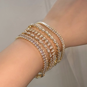 Detailed close-up of stacked gold tennis bracelets with assorted zircon stone shapes