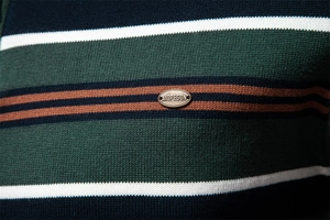 Macro shot of striped knit sweater texture with metallic brand logo detail