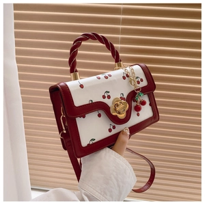 Detail of a white cherry print handbag featuring a red twisted handle and floral metal clasp