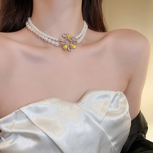 Nahaufnahme einer zweilagigen Perlenkette mit buntem Edelstein-Blumenanhänger am Modell