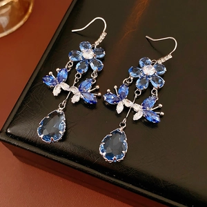 Detailed view of silver flower and butterfly earrings with blue water-drop crystals