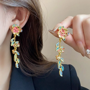 Dettaglio di orecchini floreali con petali in smalto rosa e motivi a foglia d'oro