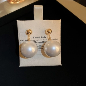 Detailed close-up of gold-plated ball stud earrings with large white pearls on a display card