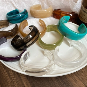 Detailed top view of wide resin bangles in various translucent colors on a ceramic plate