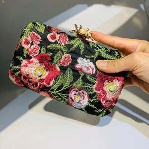 Close-up of black evening clutch with floral embroidery, pearls, and golden flower clasp