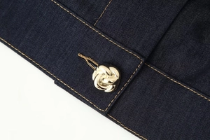 Détail du tissu denim bleu marine avec boutons dorés en métal et coutures contrastées