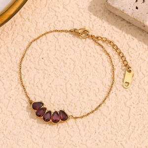 18K gold plated chain bracelet with five red pear-cut stones on a beige stone surface
