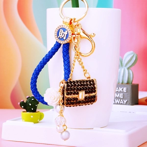 Detail of luxury pearl keychain with black rhinestone handbag and woven blue leather strap
