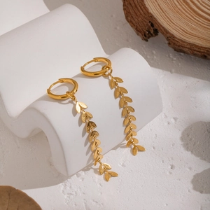 Detail shot of elegant gold leaf tassel earrings on a textured display with soft lighting