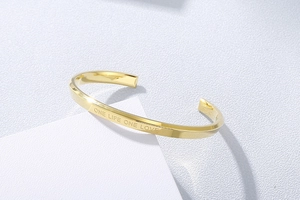 Detail of gold C-shaped cuff bracelet engraved with ONE LIFE ONE LOVE on metal