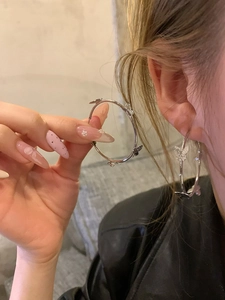 Detail showing a silver bow-knot large hoop earring worn on an ear for style display