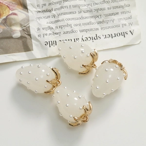Detailed view of milky white resin strawberry pendants with pearls and gold metal leaves