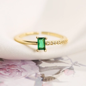 Detail of elegant emerald-cut green gemstone ring with gold band on silk fabric