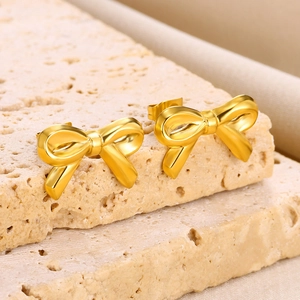 Detailed view of polished gold bow stud earrings on a textured travertine stone surface