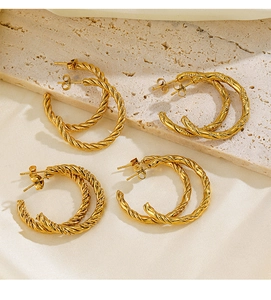 Détail de quatre boucles d'oreilles créoles dorées torsadées sur pierre et soie