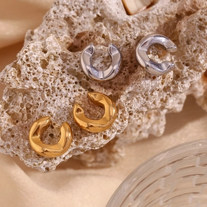 Detailed view of thick C-shape ear cuffs in polished gold and silver on stone