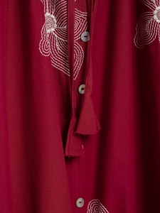 Detail of raspberry embroidered shirt with white floral patterns and tassel drawstring