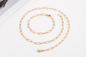 Flat lay of gold paperclip chain necklace and bracelet set on a minimal background