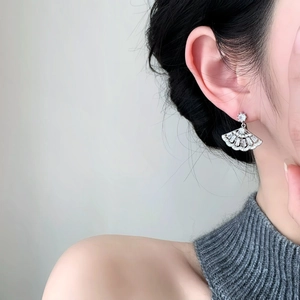 Detailed close-up of silver fan-shaped earrings with zircons worn on model ear