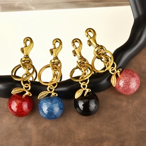 Sparkly apple-shaped keychains in red, blue, black, and pink colors on textured surface