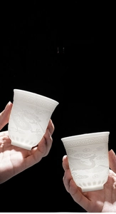 Detailed close-up of translucent Dehua white porcelain cups with embossed dragon and phoenix patterns