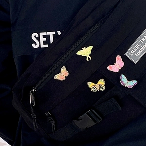 Detailed set of 5 colorful enamel butterfly pins attached to a black fabric shoulder bag