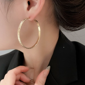 Close-up of golden round hoop earrings with textured finish worn by a fashion model