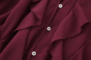 Macro shot of tiered ruffles and white buttons on a burgundy v-neck chiffon shirt