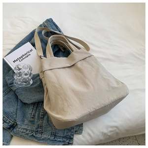 Detail of off-white large capacity nylon tote bag on a white bed sheet setup