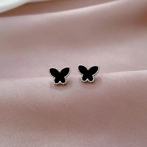 Close-up of black butterfly stud earrings with beaded edges on elegant pink silk