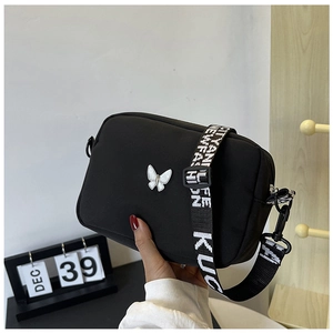 Detail of black nylon crossbody bag featuring a white butterfly buckle and lettered strap