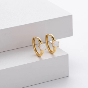 Detail of gold huggie hoop earrings with four-prong set iridescent white opal stones