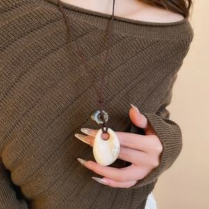 Detail of vintage cream resin oval pendant on brown cord worn over a knit sweater