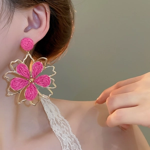 Detailansicht von rosafarbenen Bast-Ohrringen in Blumenform mit goldenem Metallrahmen