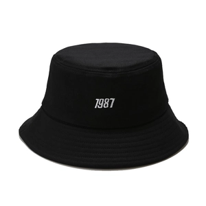 Fashionable black cotton canvas bucket hat with 1987 white embroidery on a white background