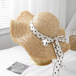 Handwoven raffia sun hat with polka dot ribbon bow on a stylish golden stand