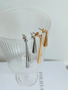 Detailed close-up of gold and silver teardrop earrings displayed on a glass rim