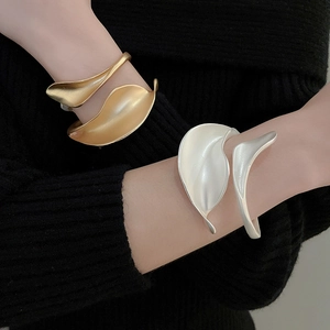 Close-up of matte gold and silver abstract leaf open cuff bracelets on model