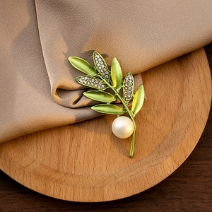 Detailed view of green enamel leaf brooch with sparkling crystals and a large pearl