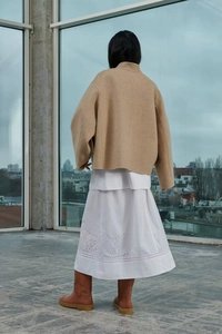 Rückansicht einer kamelfarbenen Wolljacke und eines weißen Baumwollrocks mit Stickerei