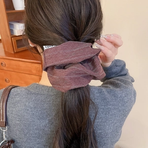Macro shot of brown herringbone fabric scrunchie with a small Jewelry brand label