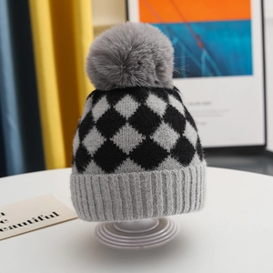 Close-up of knit texture and gray faux fur pompom on black and gray checkered baby hat