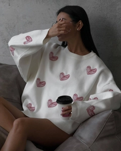 Detail of white knit sweater with red heart patterns and relaxed crew neck design
