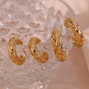 Close-up of golden hollow C-shaped croissant earrings on textured glass with satin background