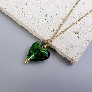 Macro detail of dark green glass heart pendant on a fine gold cross chain necklace